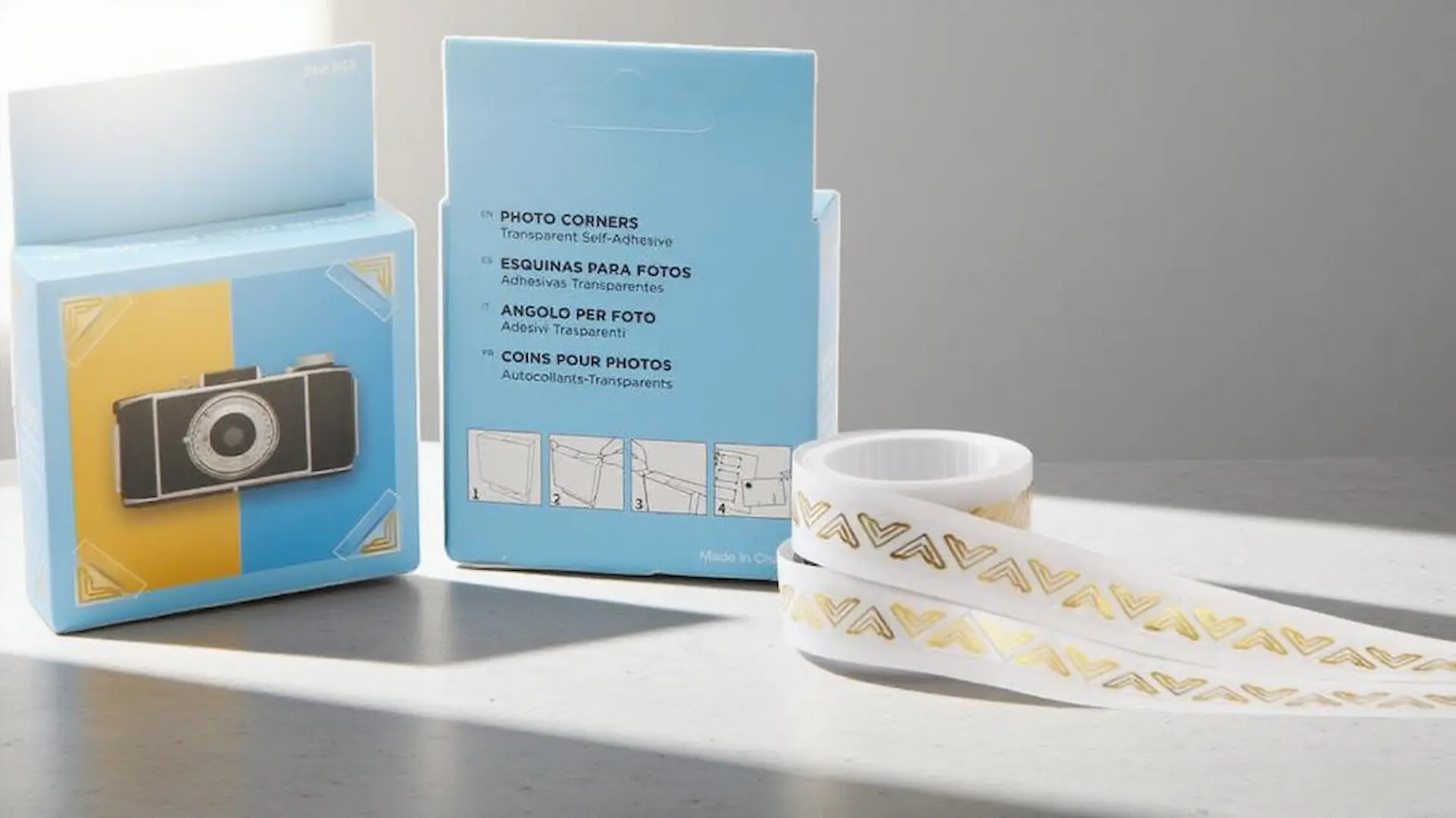 Ein professionell aufgenommenes Bild von Produktverpackungen für SENDA-Fotoecken und einer Rolle goldener Fotoecken auf einem modernen Studiotisch.